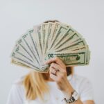 Close-up of a person holding a fan of US dollar bills on a neutral background.