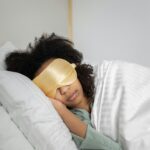 A serene scene of a black woman wearing a sleep mask, peacefully resting in bed.